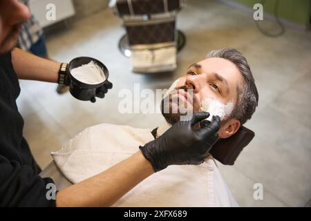 Uomo barbuto in visita a un barbiere professionista, sdraiato sulla sedia Foto Stock