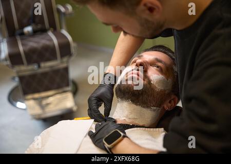 Barbiere qualificato che utilizza il rasoio dritto dopo aver applicato il gel di rasatura Foto Stock
