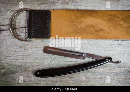 Foto in primo piano orizzontale di un rasoio dritto vintage con scaglie nere e un rasoio in pelle indossato. Superficie rustica in legno come sfondo. Foto Stock