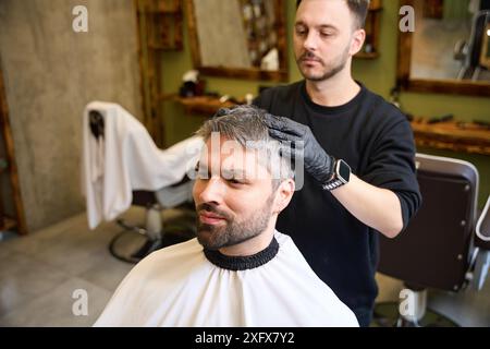 Barbiere esperto che massaggiava la testa di un cliente adulto dopo il taglio di capelli Foto Stock