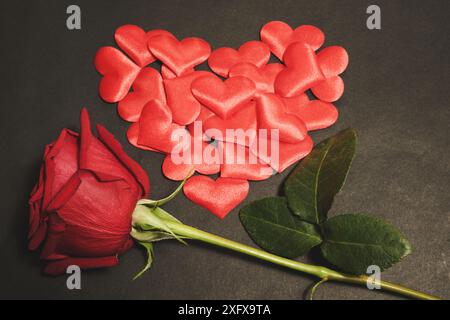 Foto orizzontale di voluttuosi cuori di rose rosse e piccoli tessuti, disposti a forma di cuore, su sfondo nero scuro. Concetto di San Valentino Foto Stock