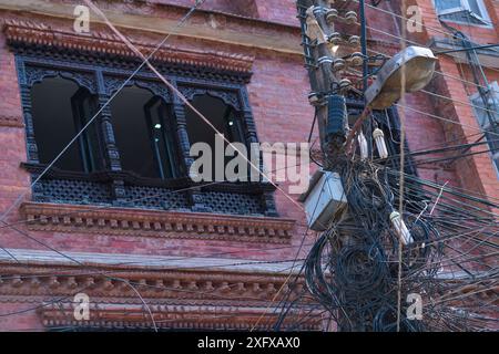 Cavi e palo telegrafico con edificio sullo sfondo, città di Kathmandu, valle di Kathmandu, Nepal. Febbraio 2018. Foto Stock