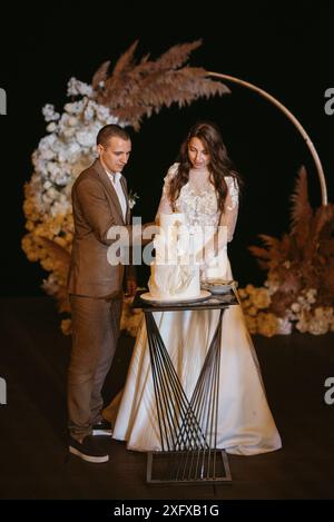 gli sposi novelli tagliano felicemente, ridono e assaggiano la torta di nozze Foto Stock