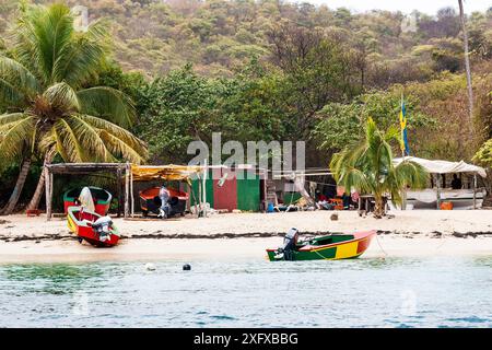 Colorata scena di spiaggia a Salt Whistle Bay, Mayreau, con molo, sarong, bar e negozio souvenir. Saint Vincent e Grenadine. Foto Stock