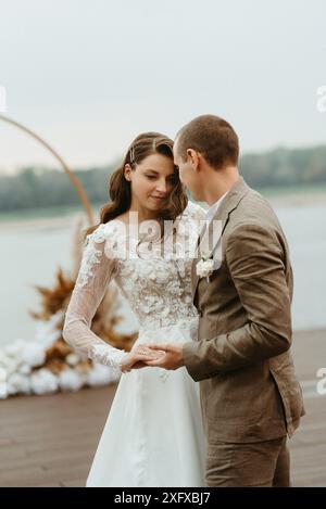 il primo ballo nuziale della sposa e dello sposo sul molo vicino al fiume, sullo sfondo dell'arco nuziale Foto Stock