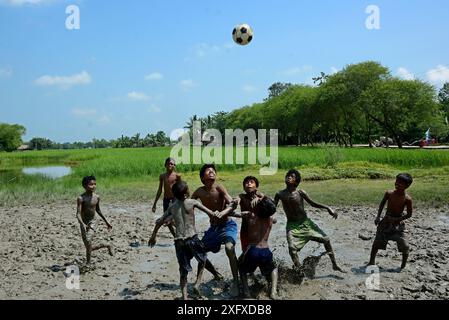 I bambini del villaggio rurale stanno giocando a calcio nel campo fangoso del villaggio di Sundarban Island, Bengala Occidentale, India. Foto Stock