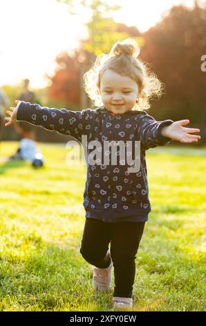 Piccola bambina gioca felice nel parco all'aperto nella primavera in controluce. Foto Stock