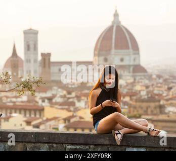 Teen al tramonto a Firenze utilizza lo smartphone, Cattedrale di Santa Maria del Fiore sullo sfondo. Foto Stock