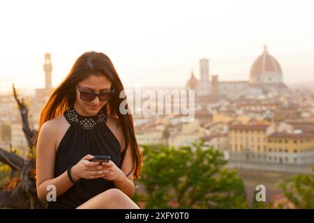 Teen al tramonto a Firenze utilizza lo smartphone, Cattedrale di Santa Maria del Fiore sullo sfondo. Foto Stock