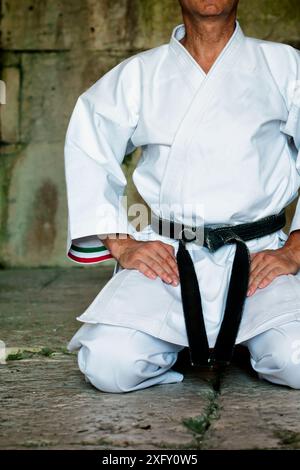 Black Belt Karate Man si siede in una posizione per iniziare o terminare la pratica. Foto Stock