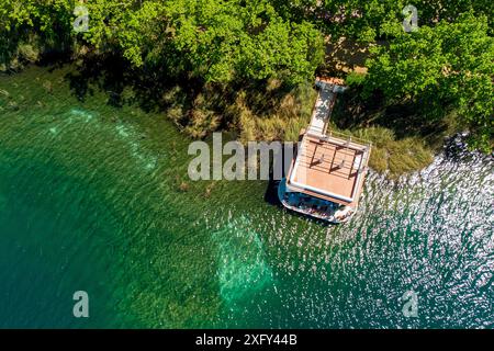 Vista aerea dall'alto verso il basso del lago Banyoles all'alba a Girona, Catalogna, Spagna. Ripresa in droni di un tranquillo paesaggio lacustre al mattino con luce calda a. Foto Stock