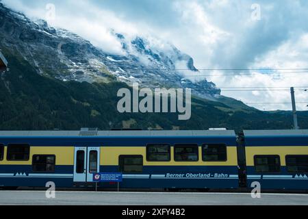 Grindelwald, Svizzera - 20 agosto 2023: Un treno che arriva alla stazione con il nuvoloso monte Eiger sullo sfondo Foto Stock