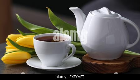 Tazza di tè caldo, teiera e tulipani sul tavolo Foto Stock