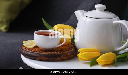 Tazza di tè caldo, fette di limone, tulipani e teiera sul tavolo in camera Foto Stock