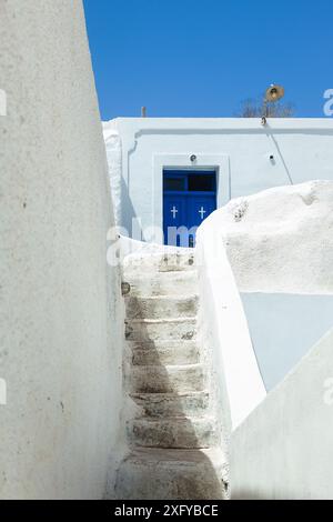 Gradini di pietra che conducono a una suggestiva porta blu di una chiesa, contro un edificio dipinto di bianco sull'isola di Thirasia, in Grecia, che mostra la bellezza delle Cicladi Foto Stock