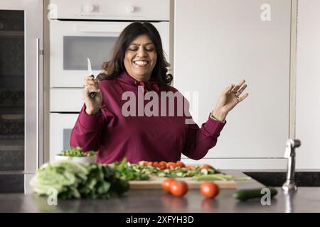 Allegra spensierata donna casalinga indiana matura che prepara la cena fatta in casa Foto Stock