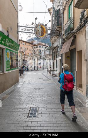 Donna con zaino che cammina dalla via dello shopping Carrer de sa Lluna (Moon Street) a Plaza de la Constitucion nel centro della città, Soller, regione di Serra de Tramuntana, Maiorca, Isole Baleari, Spagna, Europa Foto Stock