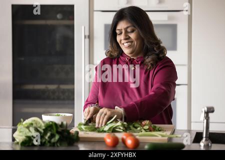 Chef indiano senior positivo che cucina insalata di verdure fresche Foto Stock