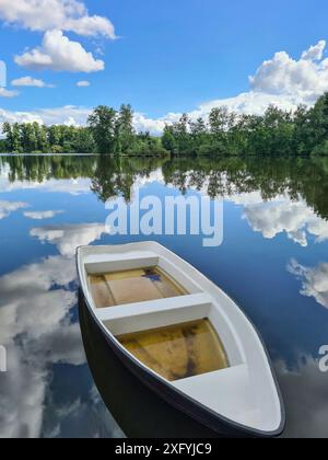 Una canoa è piena d'acqua dopo forti piogge e si trova sulla riva di un lago, l'acqua riflette le nuvole con il cielo azzurro, i cambiamenti climatici, Renania settentrionale-Vestfalia, Germania Foto Stock