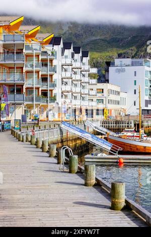 Sul lungomare della città di Svolvær, con edifici e barche moderni e colorati, montagne nebbiose sullo sfondo. Concetto di viaggio per destinazioni fredde alla moda. Foto Stock