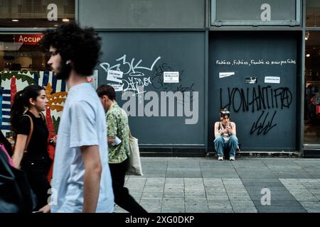 Lione, Francia. 14 giugno 2024. Liyanna, dal quartiere alternativo di sinistra di Croix Rousse, si trova di fronte a un negozio in Rue de la Republique sotto un graffito 'LYONANTIFA'. Domenica (7 luglio), sarà deciso come sarà l'Assemblea nazionale francese in futuro e chi potrebbe governare. Il Rassemblement National (RN) ha la prospettiva di assumere il governo in Francia. Crediti: Stefan Jaitner/dpa/Alamy Live News Foto Stock
