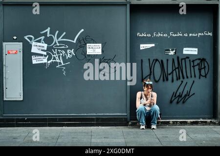 Lione, Francia. 14 giugno 2024. Liyanna, dal quartiere alternativo di sinistra di Croix Rousse, si trova di fronte a un negozio in Rue de la Republique sotto un graffito 'LYONANTIFA'. Domenica (7 luglio), sarà deciso come sarà l'Assemblea nazionale francese in futuro e chi potrebbe governare. Il Rassemblement National (RN) ha la prospettiva di assumere il governo in Francia. Crediti: Stefan Jaitner/dpa/Alamy Live News Foto Stock