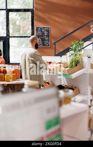 Un uomo arabo che guarda uno scaffale dove vari prodotti appena raccolti sono tenuti in scatole separate. Il cliente può scegliere tra patate, mele rosse e alcune verdure verdi. Foto Stock