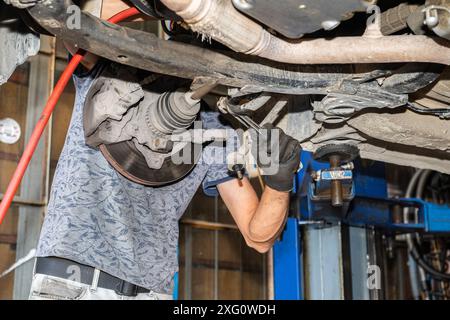 Meccanico che ripara l'auto sollevato nell'ascensore del garage. Foto Stock