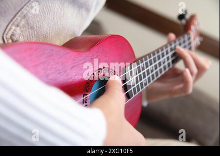 Donna con le mani gentili in cui giace un ukulele di legno rosso, primo piano. hobby hipster girl, a casa Foto Stock