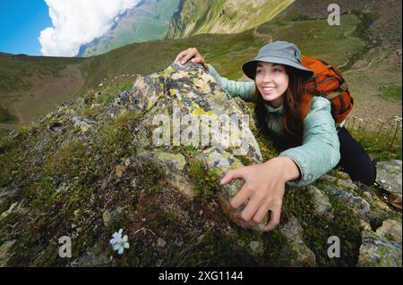 Una giovane donna turistica sorride e sale in cima alla scogliera con uno zaino. arrampicata su un ripido pendio in un profondo canyon di montagna durante le escursioni e. Foto Stock