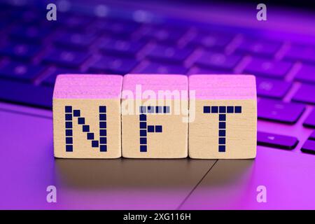 NFT parola su blocchi di legno su laptop con luci colorate. Concetto di token non fungibile Foto Stock