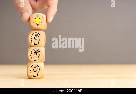 Processo di brainstorming e concetto di idea. Blocchi di legno con l'icona della testa dell'ingranaggio impilata e la mano umana che tiene la parte superiore con la lampadina Foto Stock