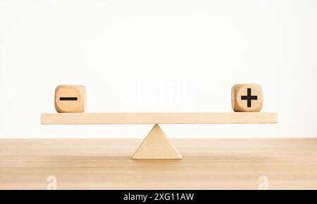 Concetto di bilanciamento Plus e Minus. Simboli positivi e negativi su blocchi di legno sono in equilibrio su una squadrina di legno. Spazio di copia Foto Stock