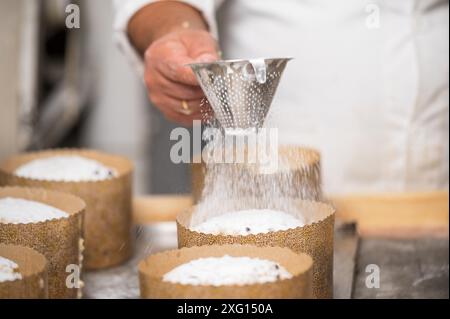 Pasticcere che condita i tradizionali panettoni italiani con zucchero a velo. Fotografia di alta qualità Foto Stock