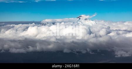 Vista panoramica della vetta innevata del vulcano LLiamna che si innalza attraverso le nuvole Foto Stock