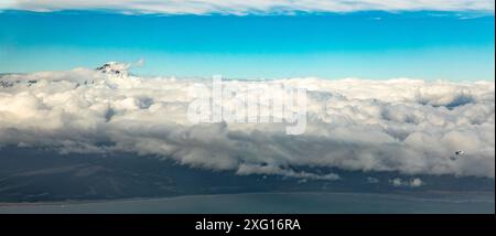 Vista panoramica di un piccolo aereo cespuglio che vola oltre la vetta del vulcano LLiamna che si innalza sopra uno strato di nuvole. Foto Stock