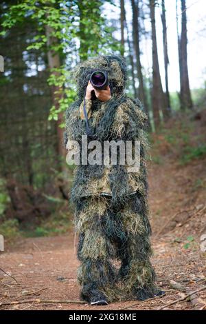 Fotografo che indossa abiti camouflage nella foresta, fotografia di animali selvatici con una macchina fotografica e teleobiettivo Foto Stock