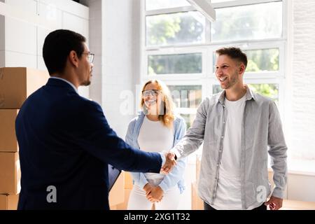 Coppia felice che celebra l'acquisto di nuove abitazioni con un agente immobiliare in ufficio, concludendo l'accordo finanziario sulla proprietà immobiliare. Foto Stock