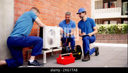 Tecnici qualificati in uniforme ispezionano le unità HVAC commerciali, conducono controlli di manutenzione e installano condizionatori d'aria per proprietari di edifici soddisfatti Foto Stock