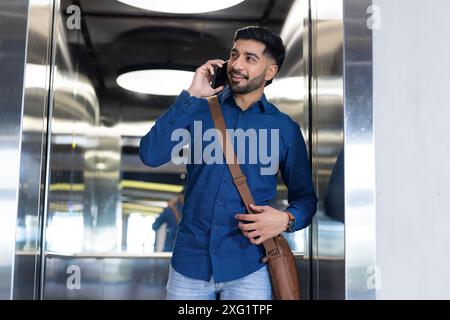 Parla sullo smartphone, uomo con borsa Messenger sorridente in ascensore Foto Stock