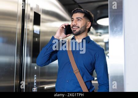 Parla sullo smartphone, uomo d'affari con la camicia blu sorridente in ascensore Foto Stock