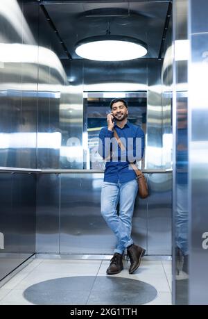 Parla con lo smartphone, uomo in un abbigliamento informale in piedi in ascensore Foto Stock