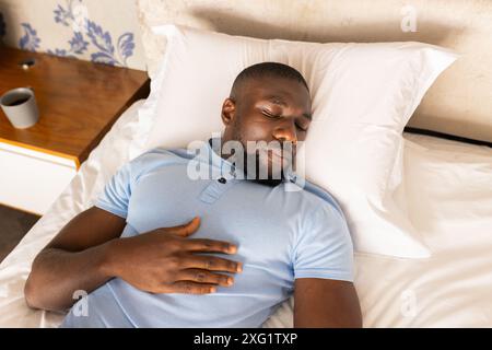 Rilassatevi a letto, uomo afroamericano che riposa mano sul petto, godendovi momenti di pace Foto Stock
