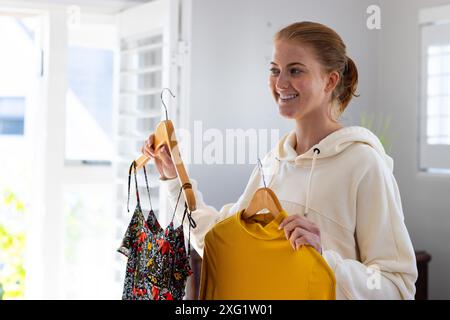 Donna sorridente con due abiti, che decide di vestirsi a casa Foto Stock