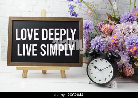 Love deep, Live Simply text message motivational and Inspiration quote con decorazioni floreali su pareti in mattoni bianchi e sfondo in legno Foto Stock