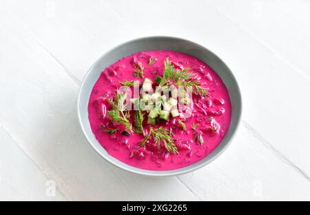 Deliziosa zuppa di barbabietole estive fredda con cetriolo e aneto nel recipiente su sfondo bianco in legno. Disintossicazione sana o concetto di cibo vegetariano. Vista ravvicinata Foto Stock