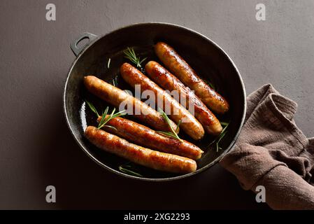 Vista ravvicinata di deliziose salsicce sottili nella padella su sfondo di pietra scura. Foto Stock