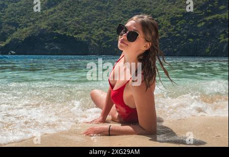 Giovane donna che si rilassa su una spiaggia tropicale con un costume da bagno rosso Foto Stock