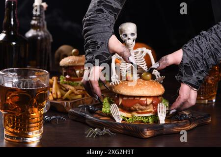 Le mani delle streghe vogliono prendere il Monster Burger sullo scheletro seduto. Perfetto antipasto per la festa di Halloween Foto Stock