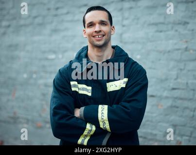 Pompiere, braccia incrociate e felice per il ritratto in città con uniforme di sicurezza, orgoglio e carriera in servizio. Persona, sorriso e attrezzatura riflettente per il salvataggio Foto Stock